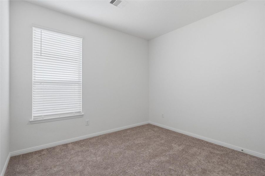 This secondary bedroom offers comfort and style with plush carpeting, neutral paint tones, a large window with blinds, and a generously sized closet.
