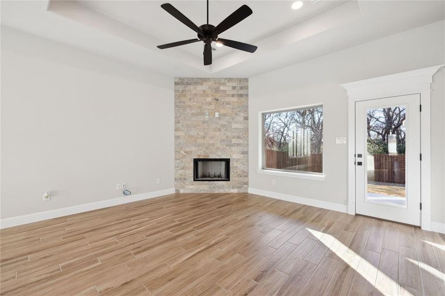 Unfurnished living room featuring a raised ceiling, a stone fireplace, and ceiling fan