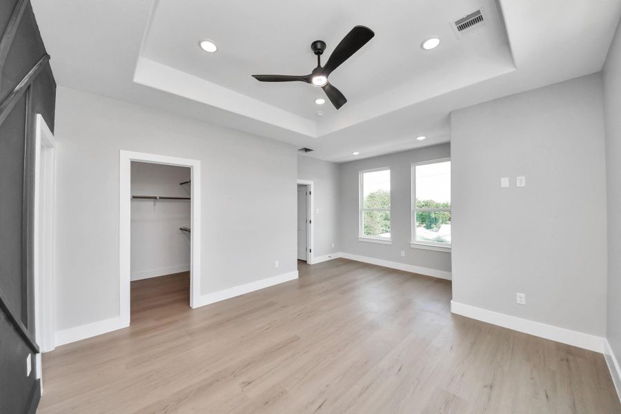 Spacious primary bedroom featuring tray ceilings, oversized windows, abundant natural light, & modern finishes throughout.