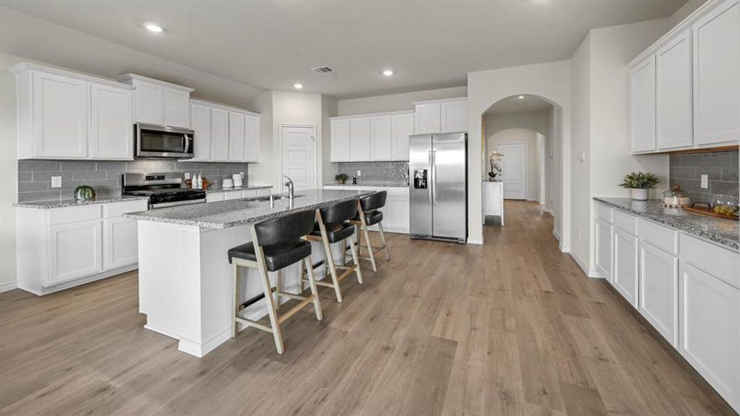 Kitchen with arched walkways, white cabinets, backsplash, stainless steel appliances, and a breakfast bar area