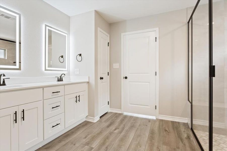 Full bathroom featuring double vanity, wood finished floors, and a shower stall Full bathroom featuring double vanity, wood finished floors, and a shower stall