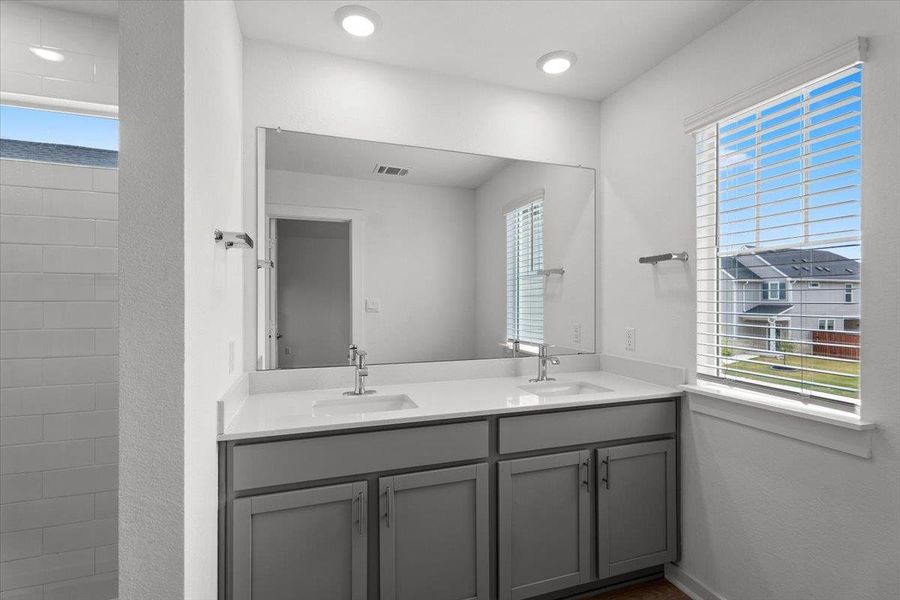 A well-appointed primary bathroom features dual vanities, modern fixtures, and a naturally illuminated shower.