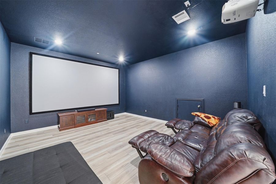 Entertainment room featuring a large projection screen, recessed lighting, and light-toned flooring