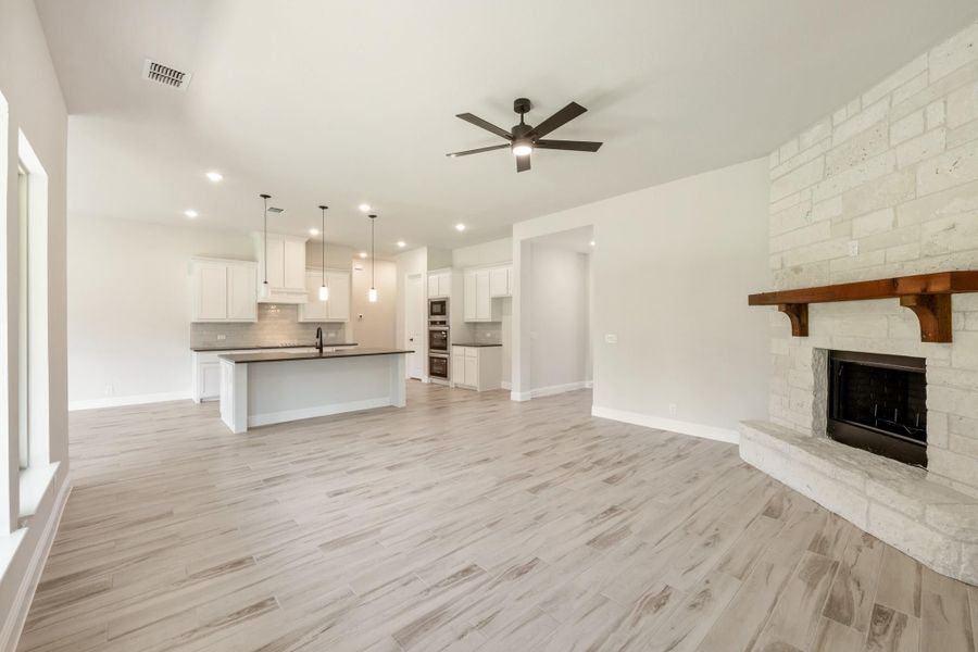 Open living area with stone fireplace, ceiling fan, and kitchen with white cabinets and center island