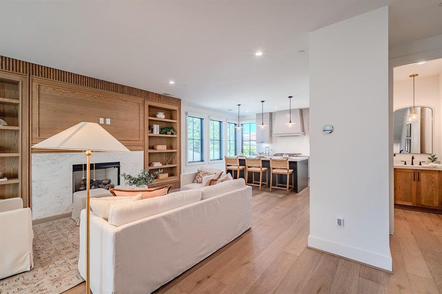 Living room with built in shelves, a premium fireplace, light wood-style flooring, and recessed lighting