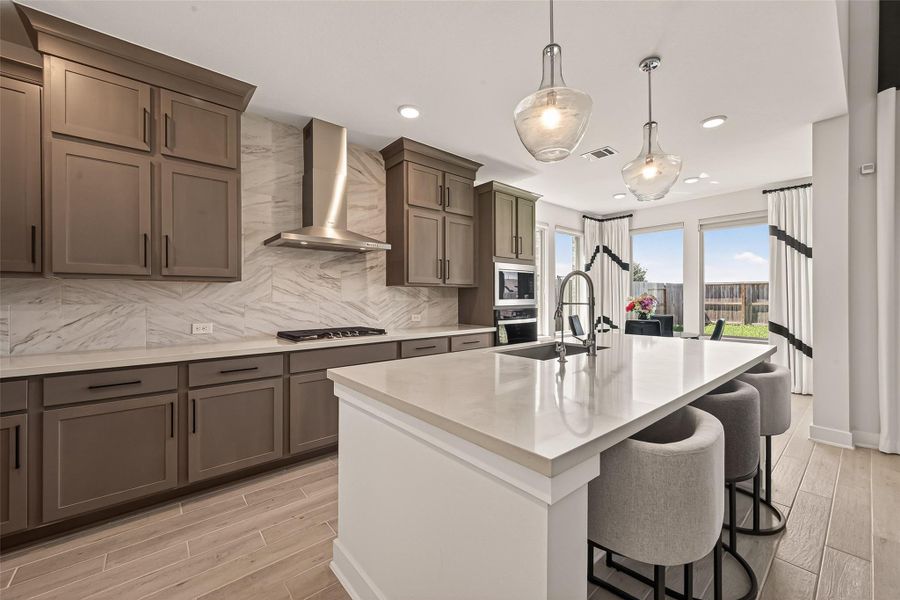 This modern kitchen features sleek cabinetry, a large island with seating, stainless steel appliances, and ample natural light from the adjacent dining area with large windows overlooking the backyard.