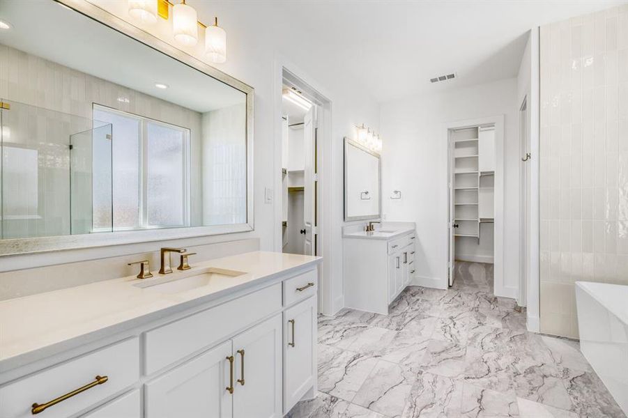 Full bathroom with a shower stall, a walk in closet, two vanities, a soaking tub, and light marble finish floors