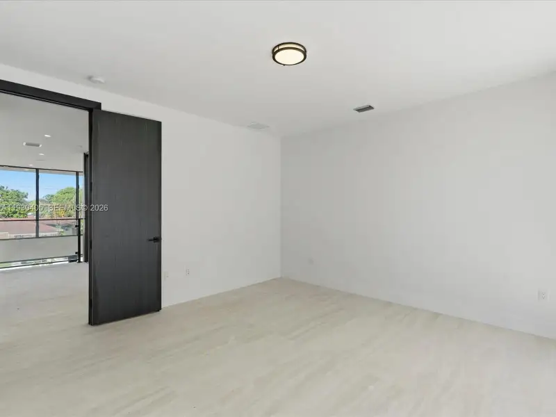 Neutral-toned stone flooring, dark-stained wood door with matte black hardware, and a modern circular ceiling-mounted light fixture Neutral-toned stone flooring, dark-stained wood door with matte black hardware, and a modern circular ceiling-mounted light fixture