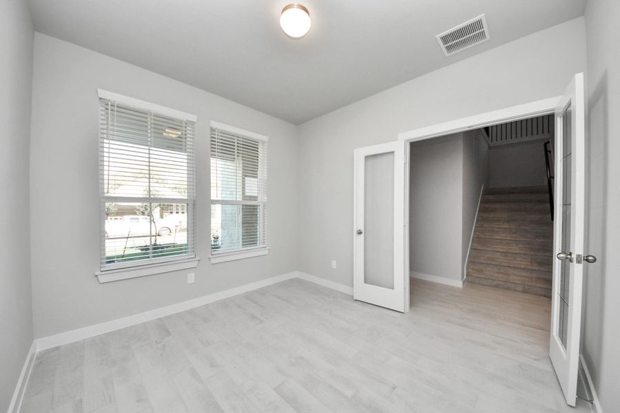 Experience the perfect blend of sophistication and warmth in this home office, boasting elegant wood-look tile flooring and flooded with natural light from expansive windows and French doors. Sample photo of completed home with similar floor plan. Actual colors and selections may vary.