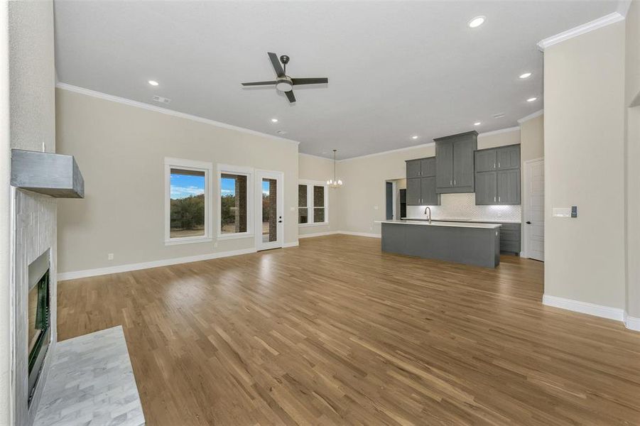 Unfurnished living room featuring a tile fireplace, crown molding, ceiling fan with notable chandelier, and hardwood / wood-style flooring