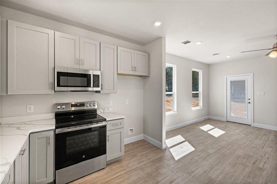 Kitchen with light hardwood / wood-style floors, appliances with stainless steel finishes, ceiling fan, and light stone countertops