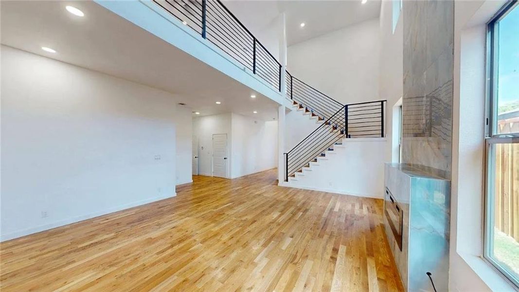 Open-concept living area featuring high ceilings, wood-finish flooring, a modern linear fireplace with a stone surround, and a floating staircase with metal railings