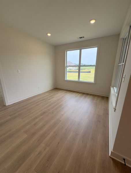 Room featuring wood-finish flooring, recessed ceiling lighting, a large double-pane window, and white baseboards