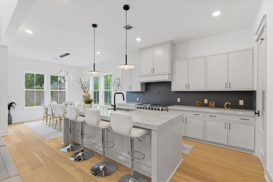 The kitchen features two pendant lights and an island with additional seating for guests. It flows seamlessly into the dining area, highlighted by a modern light fixture and abundant windows.