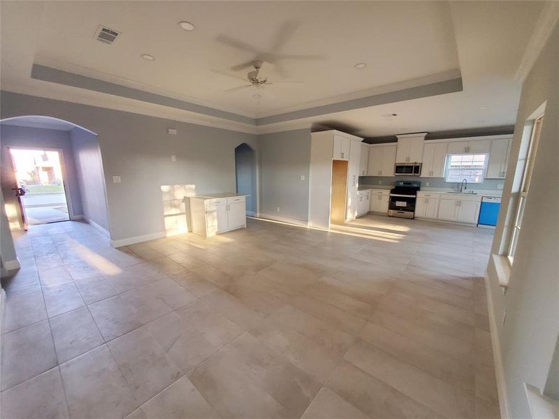 Unfurnished living room featuring ceiling fan, a raised ceiling, sink, and crown molding