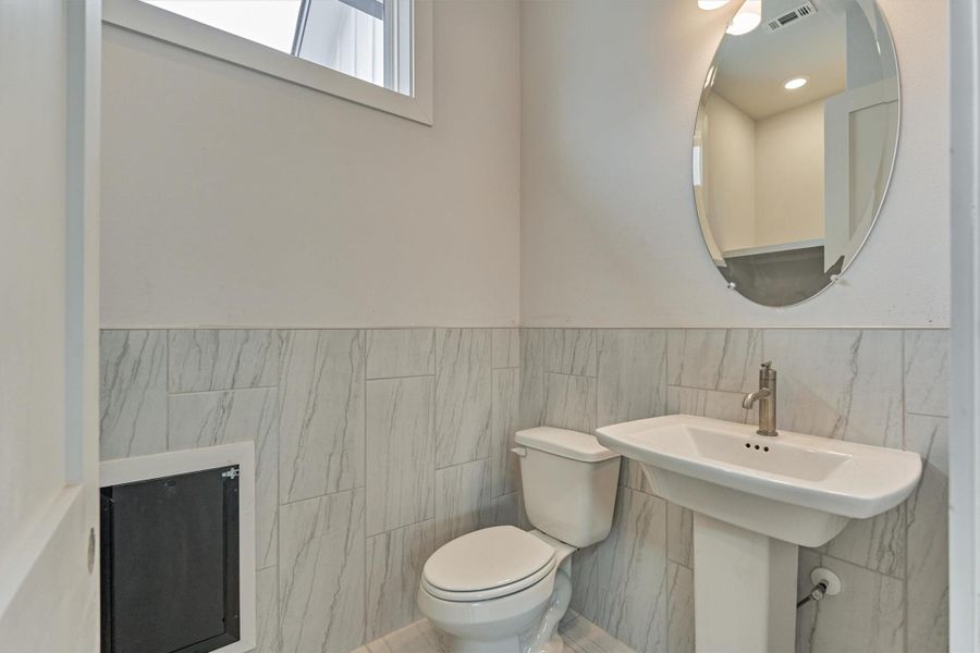 Convenient half bath featuring sleek pedestal sink, modern fixtures, and easy-care tile—perfectly designed for quick cleanups and everyday practicality.