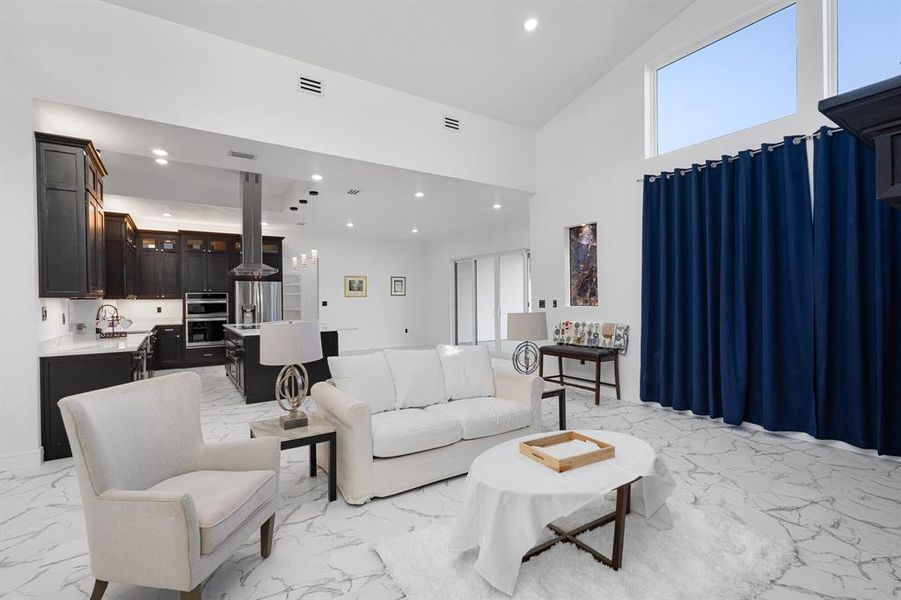 Living area featuring plenty of natural light, light marble finish flooring, recessed lighting, and a high ceiling