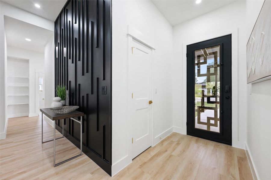 Entryway featuring a decorative black paneled accent wall, a black entry door with geometric glass inserts, light wood-finish flooring, and recessed ceiling lighting