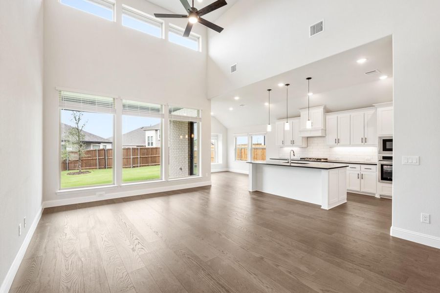 Open living area with high ceilings and hardwood floors flowing into white kitchen with island and pendant lights Open living area with high ceilings and hardwood floors flowing into white kitchen with island and pendant lights