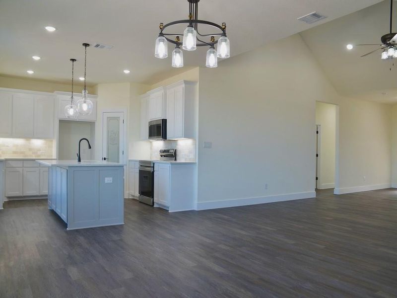 Kitchen with hanging light fixtures, white cabinetry, stainless steel appliances, and a kitchen island with sink