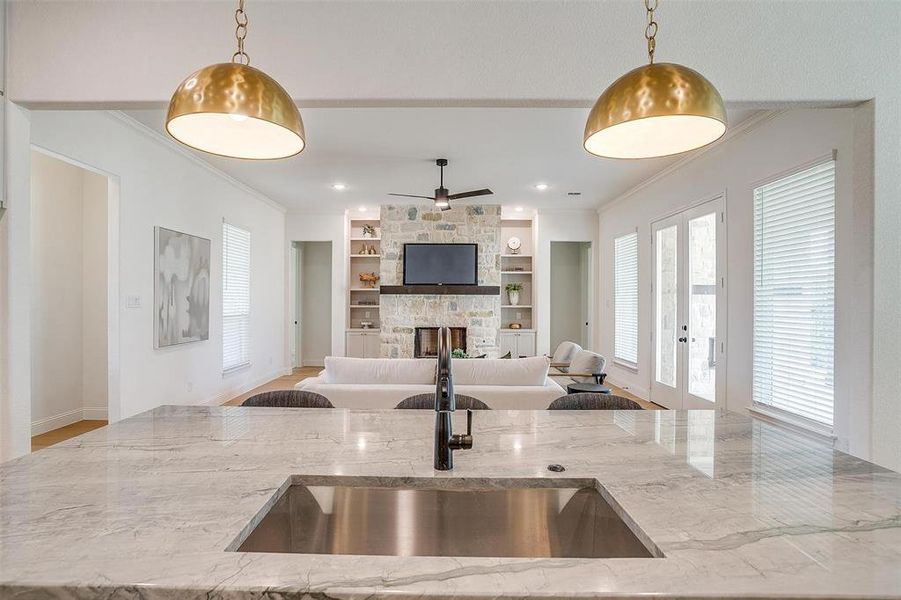 Kitchen featuring built in shelves, ceiling fan, light stone countertops, a fireplace, and decorative light fixtures