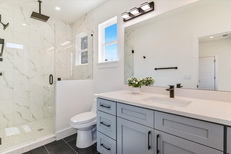 Start your day in luxury. The primary bath boasts a walk-in shower with floor-to-ceiling marble-patterned tile, a rainfall showerhead, and a sprawling vanity with designer matte black fixtures.