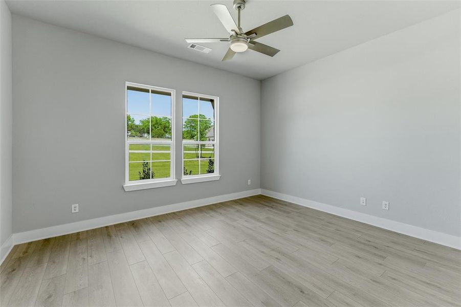 Spacious room featuring wood-finish flooring, two large windows with white trim, a contemporary ceiling fan with integrated lighting, and neutral wall tones