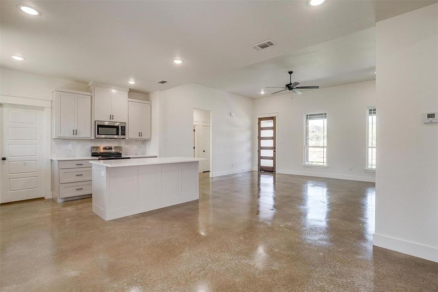 Kitchen featuring appliances with stainless steel finishes, a kitchen island, backsplash, white cabinetry, and ceiling fan