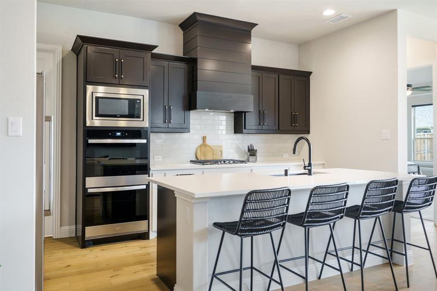 Kitchen with stainless steel appliances, a sink, a kitchen island with sink, light wood-type flooring, and decorative backsplash Kitchen with stainless steel appliances, a sink, a kitchen island with sink, light wood-type flooring, and decorative backsplash
