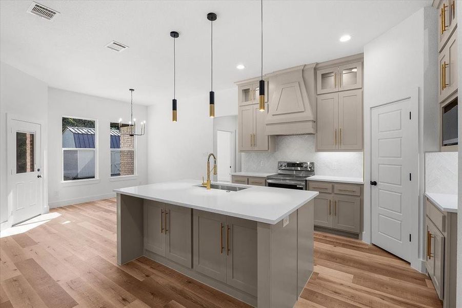 Kitchen featuring stainless steel electric range oven, sink, a kitchen island with sink, and light hardwood / wood-style flooring