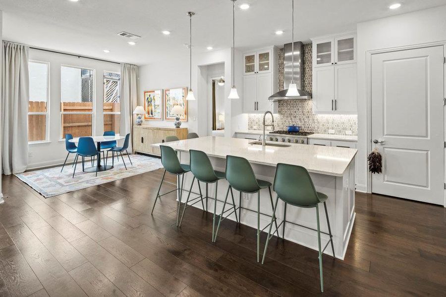 Kitchen featuring a center island with sink, light countertops, decorative backsplash, wall chimney exhaust hood, and a sink