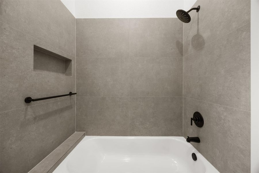 Designer tile with built-in niche and matte black fixtures complete this full bathroom.