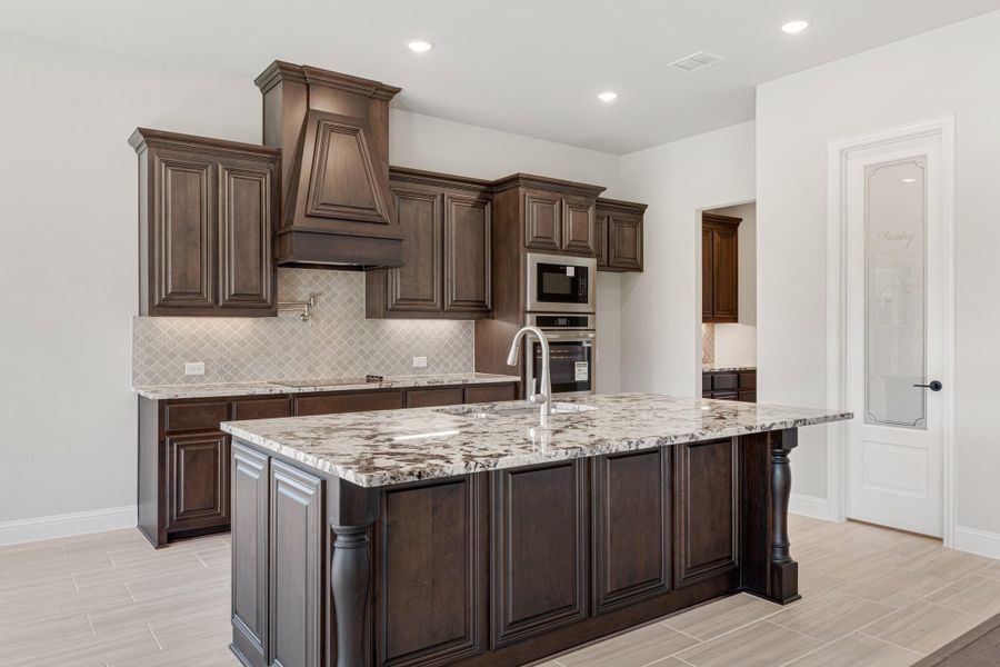 Kitchen with dark wood cabinets, granite island, custom range hood, and stainless steel appliances Kitchen with dark wood cabinets, granite island, custom range hood, and stainless steel appliances