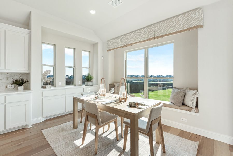 Bright dining area with wood table, built-in window bench seat, and hardwood floors next to white kitchen cabinets