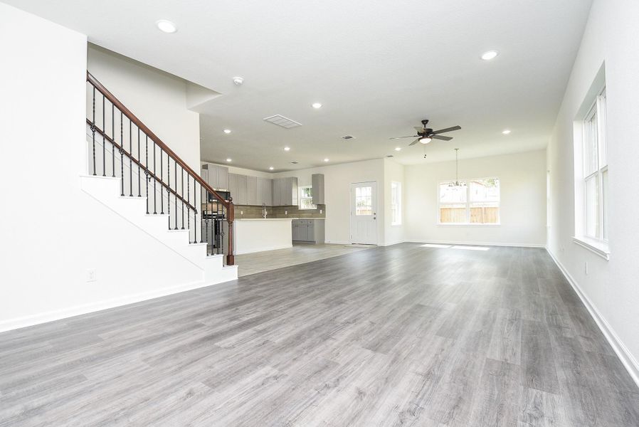 This is a spacious, bright room with contemporary gray flooring, large windows for natural light, a ceiling fan for comfort, and a staircase leading to the upper level. The neutral color palette offers a versatile backdrop for a variety of decor styles. This is a spacious, bright room with contemporary gray flooring, large windows for natural light, a ceiling fan for comfort, and a staircase leading to the upper level. The neutral color palette offers a versatile backdrop for a variety of decor styles.