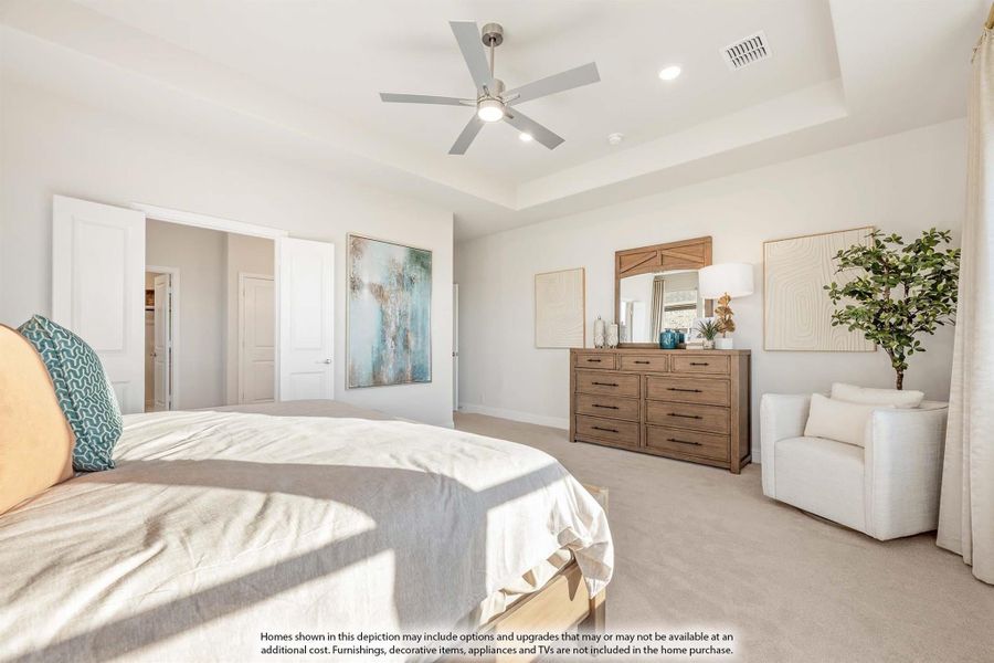 Spacious master bedroom with tray ceiling, ceiling fan, wood dresser, and walk-in closet access on carpet flooring Spacious master bedroom with tray ceiling, ceiling fan, wood dresser, and walk-in closet access on carpet flooring