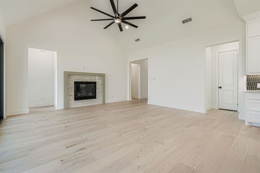 Unfurnished living room featuring high vaulted ceiling, light wood finished floors, a glass covered fireplace, and ceiling fan Unfurnished living room featuring high vaulted ceiling, light wood finished floors, a glass covered fireplace, and ceiling fan