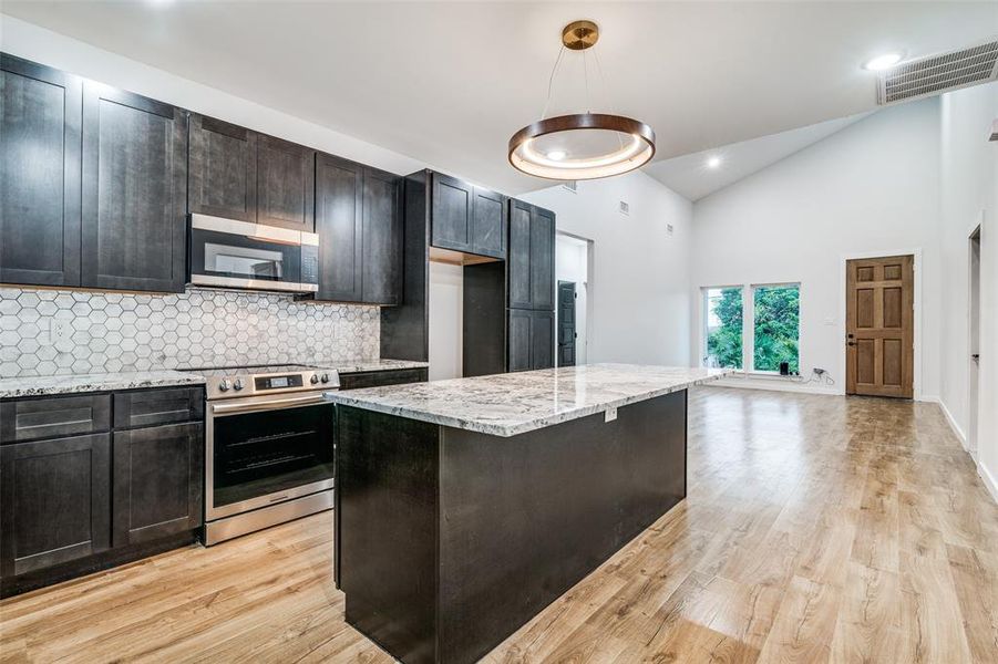 Kitchen featuring stainless steel appliances, light hardwood / wood-style floors, light stone counters, a center island, and pendant lighting