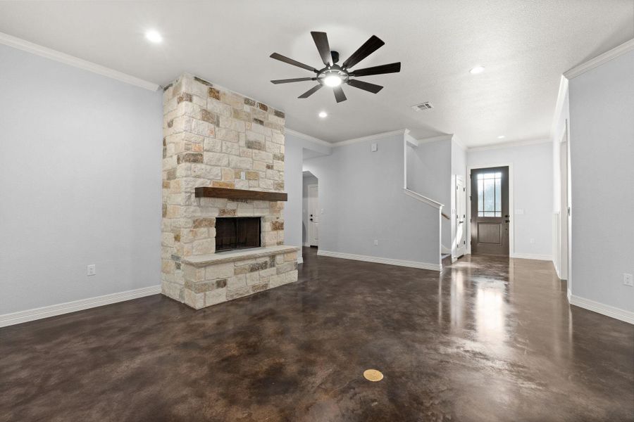 Unfurnished living room featuring finished concrete flooring, crown molding, a stone fireplace, a ceiling fan, and arched walkways