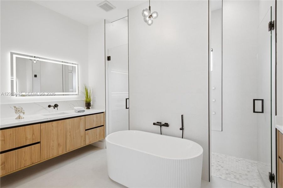 Spa-inspired primary bathroom features a freestanding soaking tub framed by dual floating vanities with illuminated mirrors. Spa-inspired primary bathroom features a freestanding soaking tub framed by dual floating vanities with illuminated mirrors.