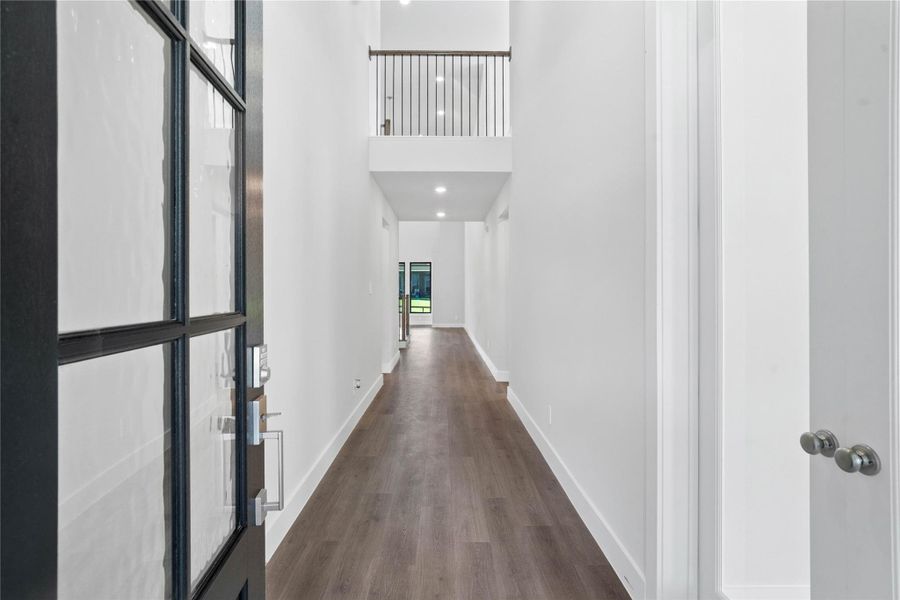 Step inside to a bright interior entryway. The space is accentuated by high, 2-story ceilings and gorgeous LVP flooring. The hallway extends toward large windows at the rear, flooding the area with natural light.