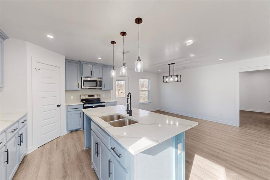 Kitchen with appliances with stainless steel finishes, a kitchen island with sink, sink, light hardwood / wood-style floors, and hanging light fixtures