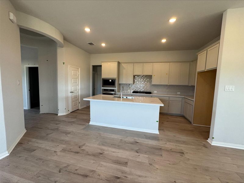Kitchen featuring a kitchen island with sink, light countertops, arched walkways, light wood-style floors, and tasteful backsplash Kitchen featuring a kitchen island with sink, light countertops, arched walkways, light wood-style floors, and tasteful backsplash