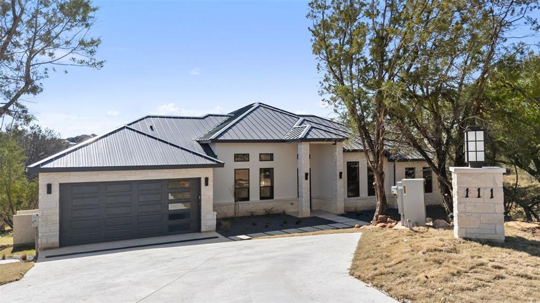 View of front of home with a standing seam roof, a metal roof, driveway, and stone siding View of front of home with a standing seam roof, a metal roof, driveway, and stone siding