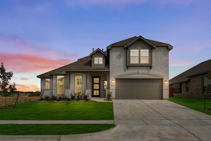 Two-story brick home with two-car garage, covered entry, and green front lawn at dusk