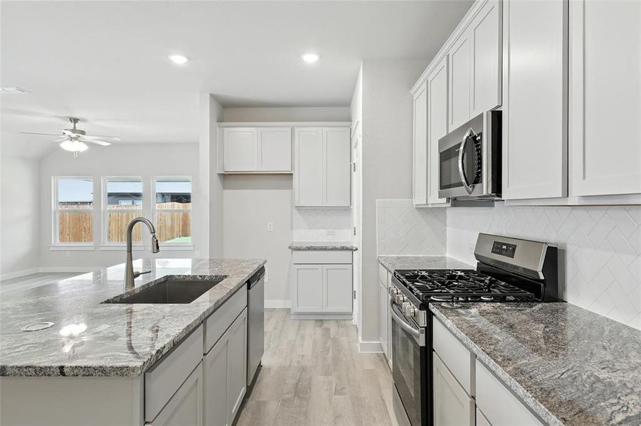 Kitchen with stainless steel appliances, backsplash, a ceiling fan, a kitchen island with sink, and light wood-type flooring