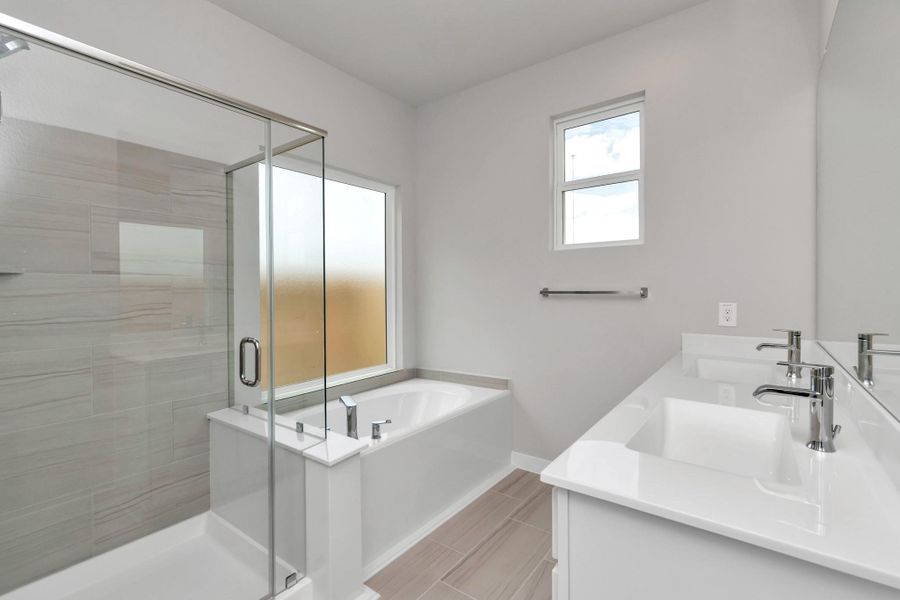 Enjoy the roomy walk-in shower encased in stylish tile, take a moment to unwind in a separate garden tub embellished with custom details, and elevate your daily routine at the refined vanity, now boasting double sinks, light-toned countertops, modern hardware, and bright recessed lights. Sample photo of completed home with similar floor plan. Actual colors and selections may vary.