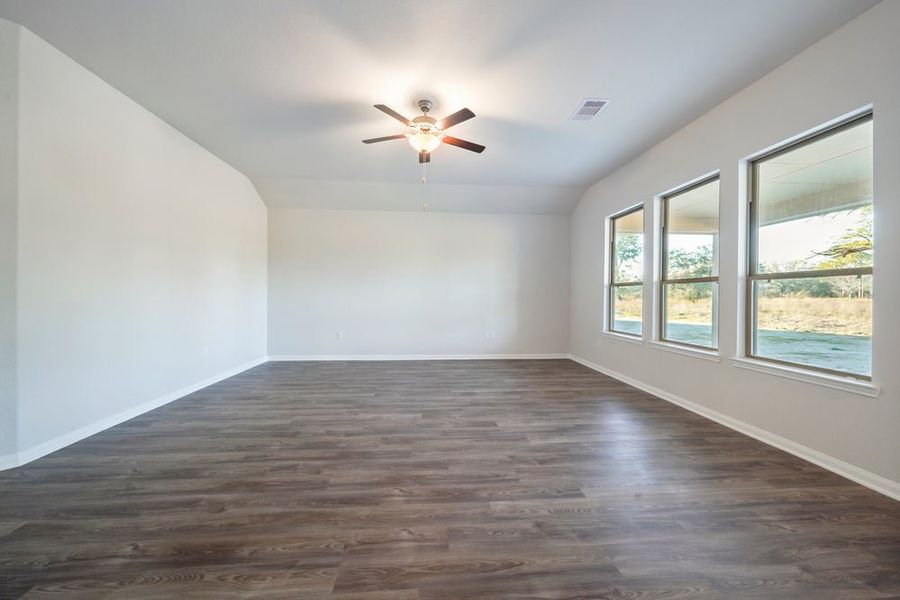 Empty room with dark hardwood floors, vaulted ceiling, ceiling fan, and three windows