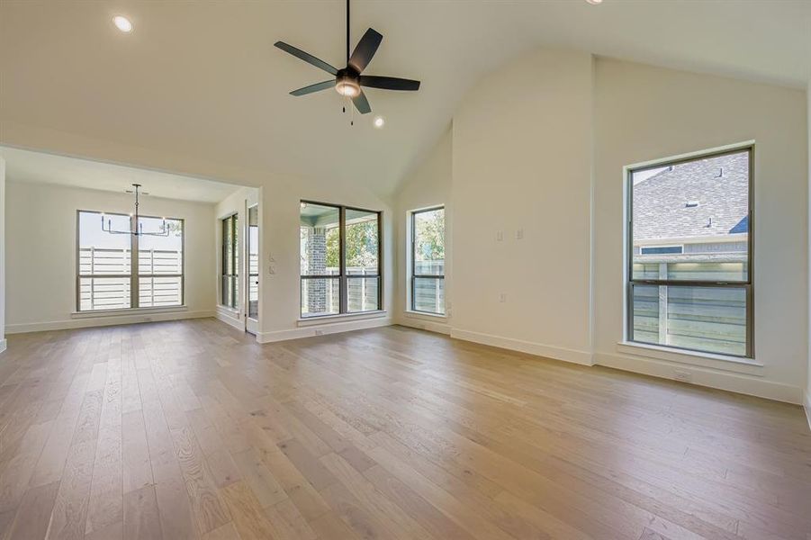 Unfurnished living room featuring recessed lighting, light wood-type flooring, high vaulted ceiling, a ceiling fan, and a chandelier Unfurnished living room featuring recessed lighting, light wood-type flooring, high vaulted ceiling, a ceiling fan, and a chandelier
