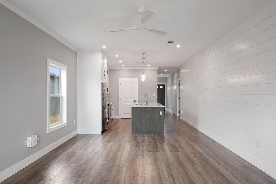 Kitchen featuring pendant lighting, a center island with sink, crown molding, dark wood-type flooring, and a ceiling fan